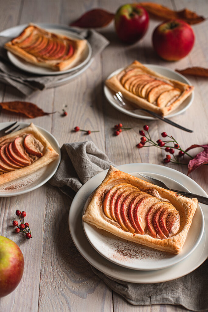 Blätterteig-Apfelteilchen auf Tellern auf herbstlich gedecktem Holztisch