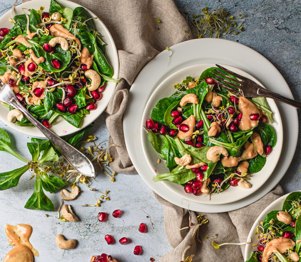 Feldsalat auf Tellern mit Granatapfelkernen und Dressing