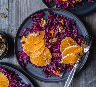 Rotkohl-Orangen-Salat mit Walnüssen auf dunkelgrauem Teller angerichtet