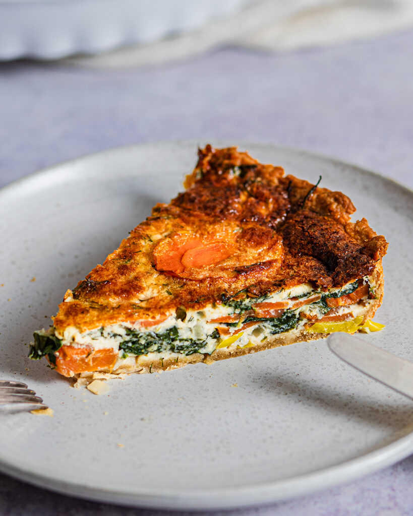 Möhren-Spinat-Quiche auf hellem Teller mit Besteck