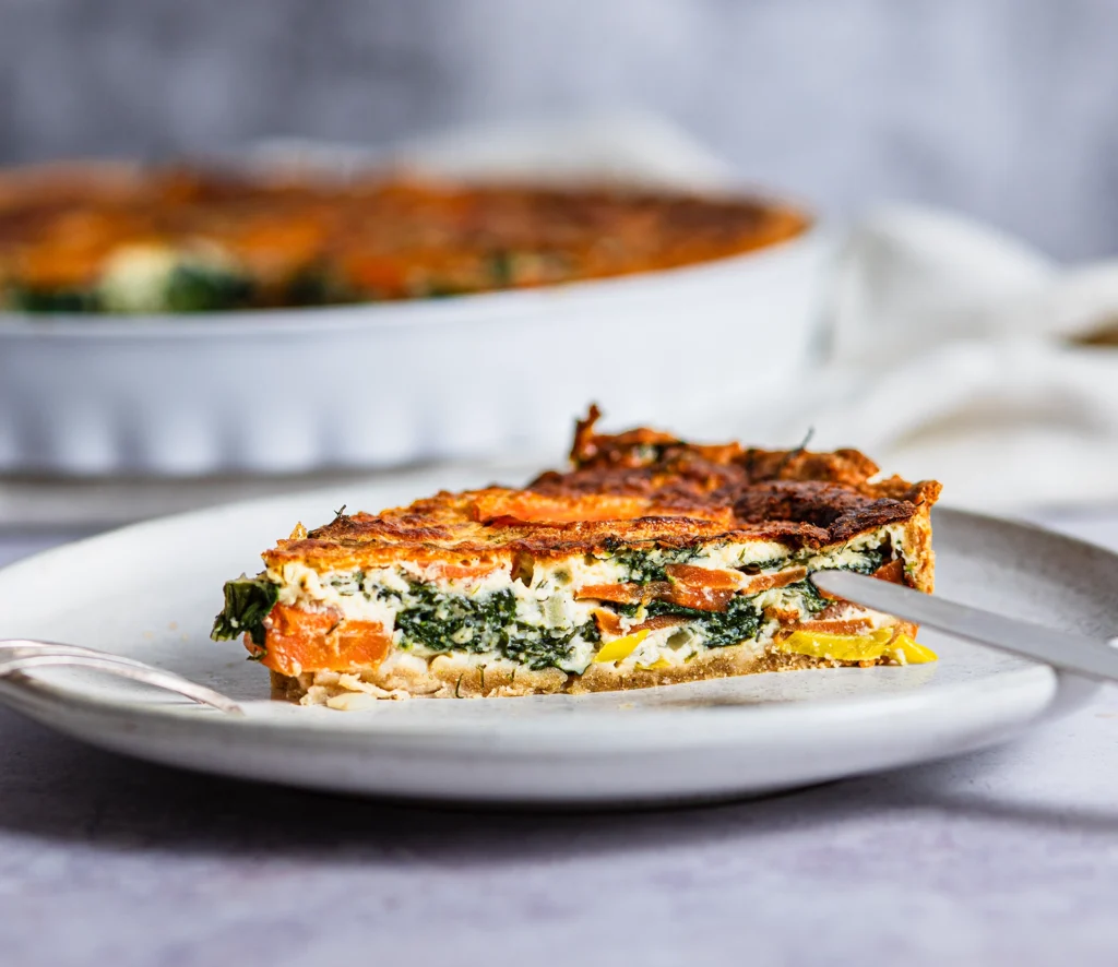 Ein Stück Möhren-Spinat-Quiche auf hellem Teller
