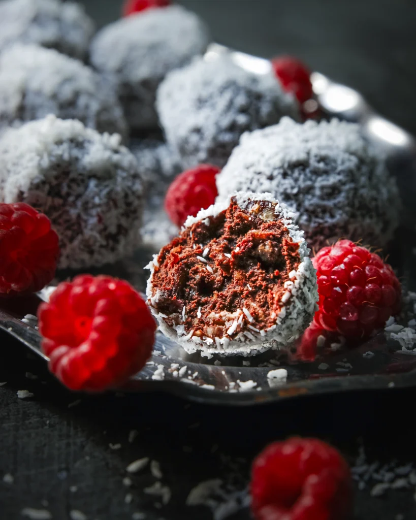Nahaufnahme von schwedischen Chokladbollar mit Himbeeren – schokoladige Haferkugeln mit frischen Himbeeren, auf dunklem Untergrund und silbernen kleinen Tablett