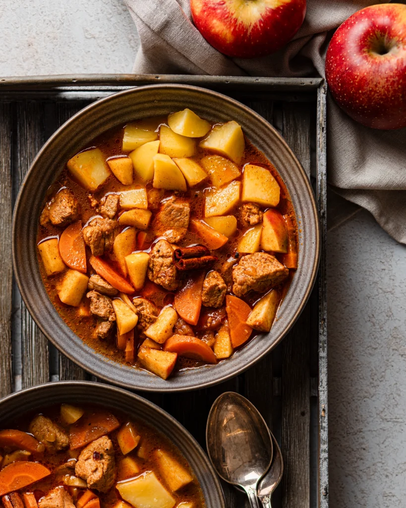 Herbstliches Gulasch mit Apfel und Zimt auf 2 Tellern auf einem Holztablett